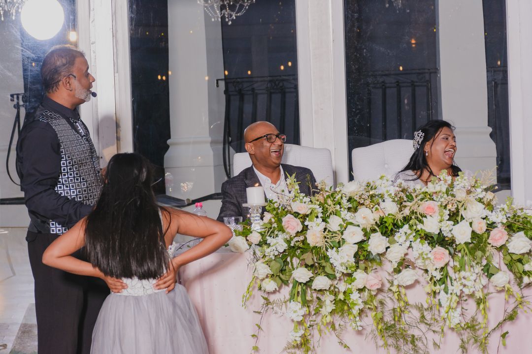 Nichal Sarawan hosting a wedding reception, addressing the laughing bride and groom