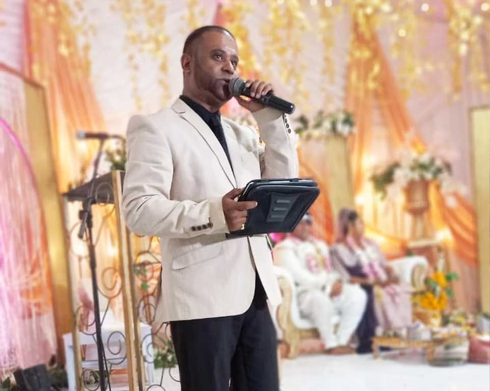 Nichal Sarawan hosting a celebration, microphone in hand with guests in the background